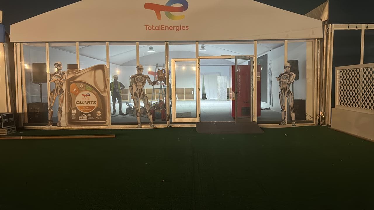 Illuminated TotalEnergies tent facade at night with the logo, glass front and Quartz product display inside